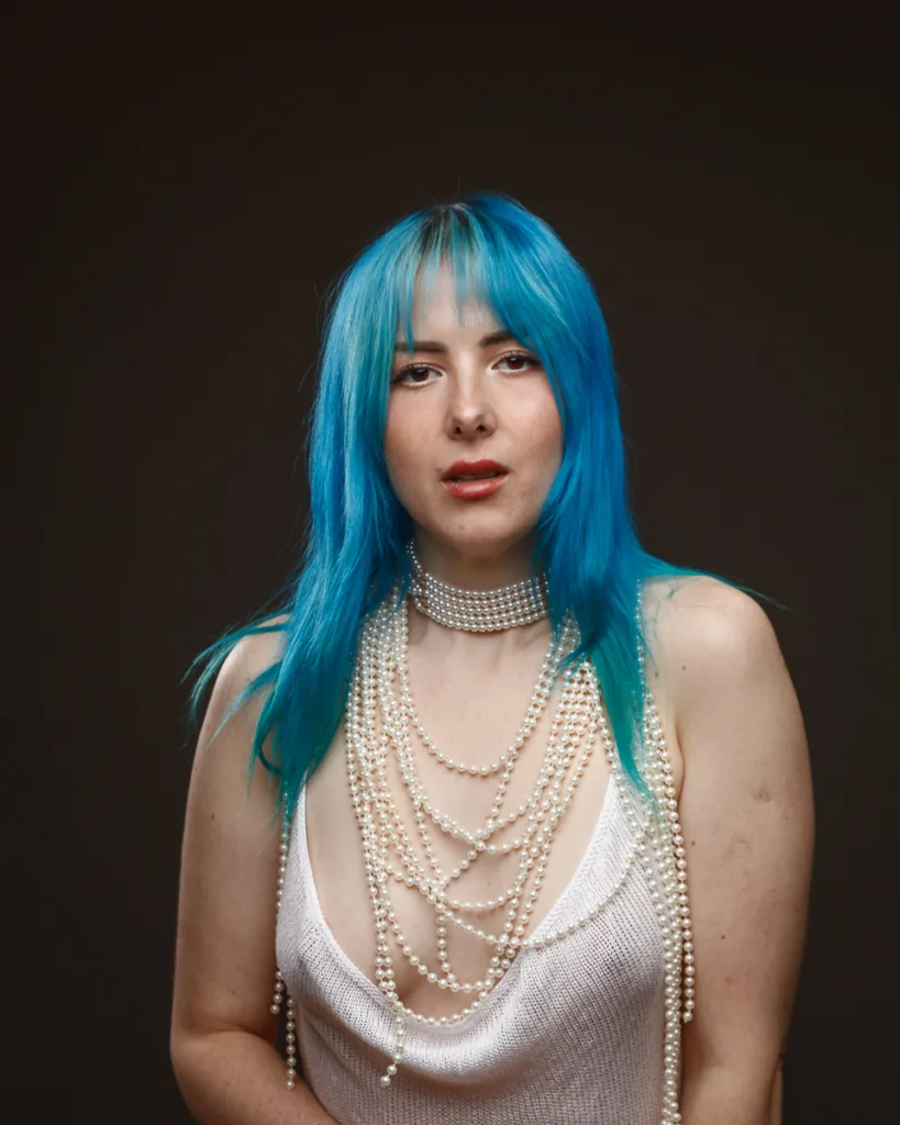 Person with blue hair, wearing pearl necklace.
