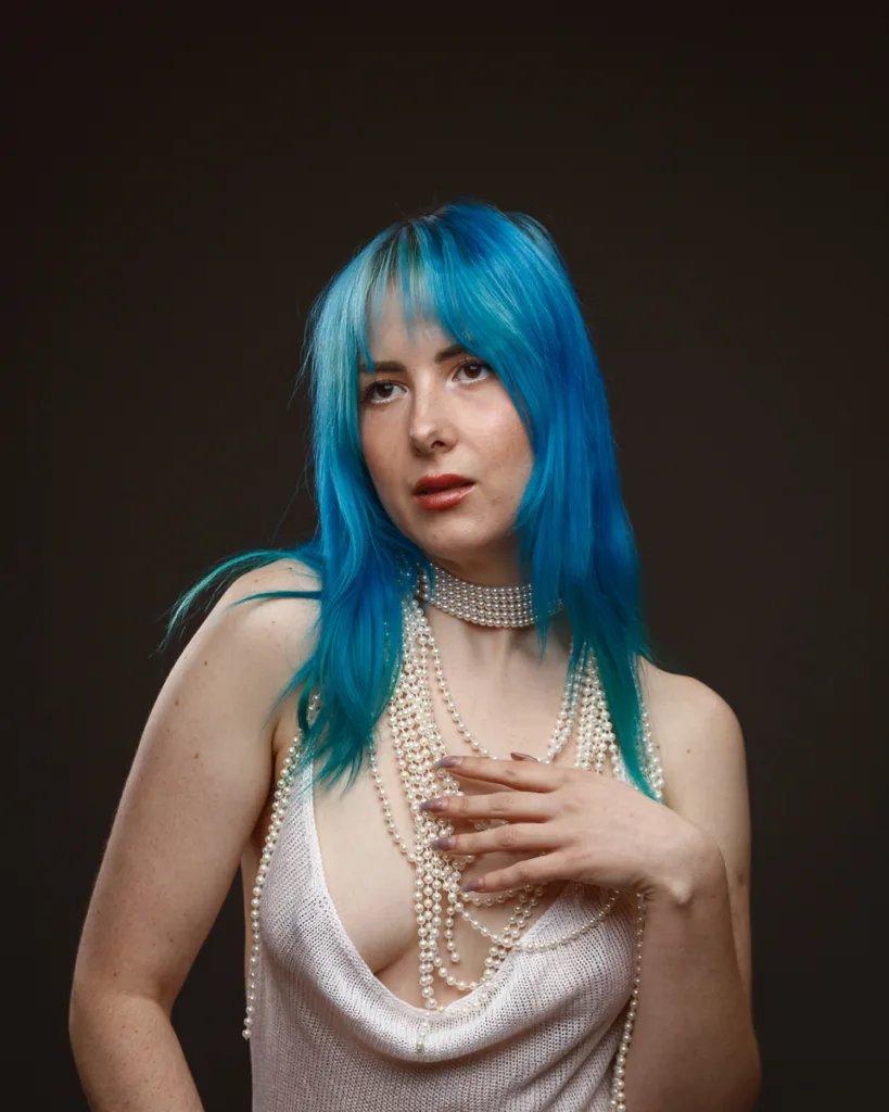 Person with blue hair wearing pearl accessories.