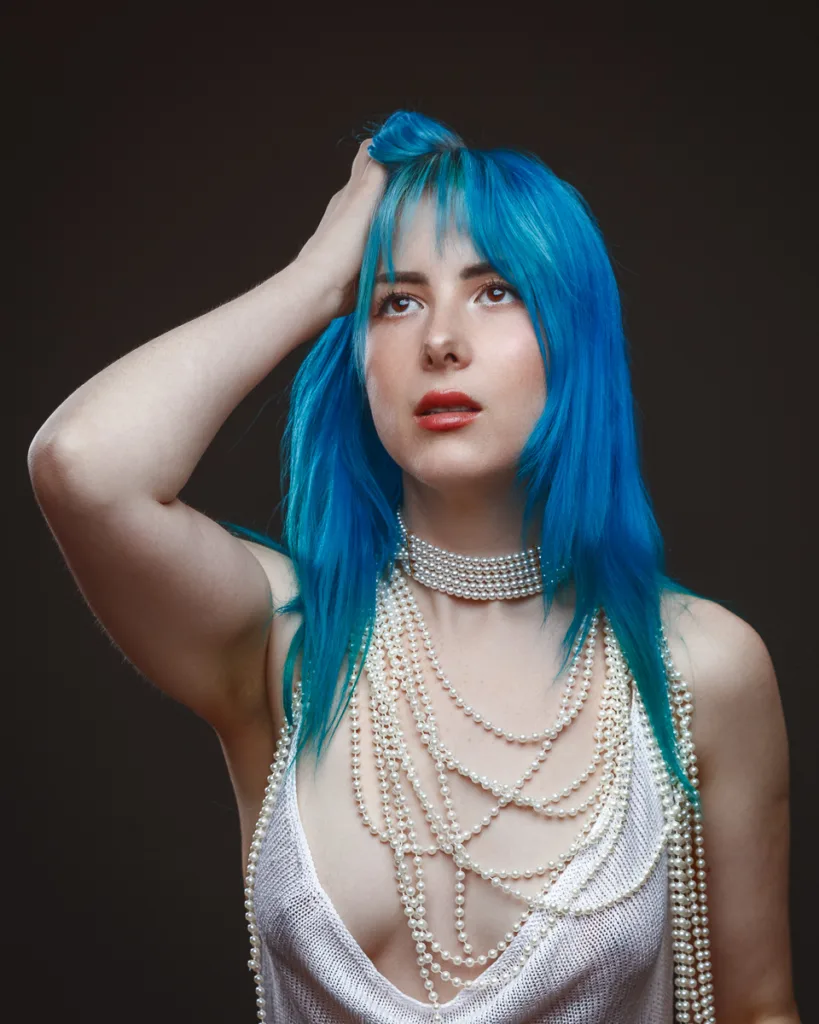 Woman with blue hair and pearl necklaces.
