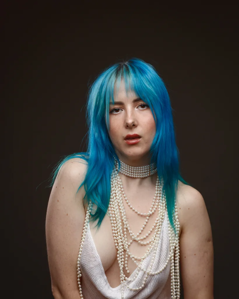 Person with blue hair and pearl accessories
