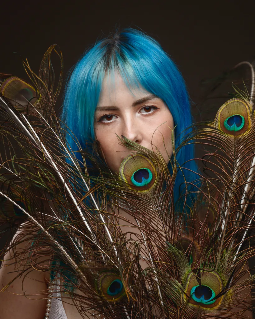 Person with blue hair and peacock feathers.