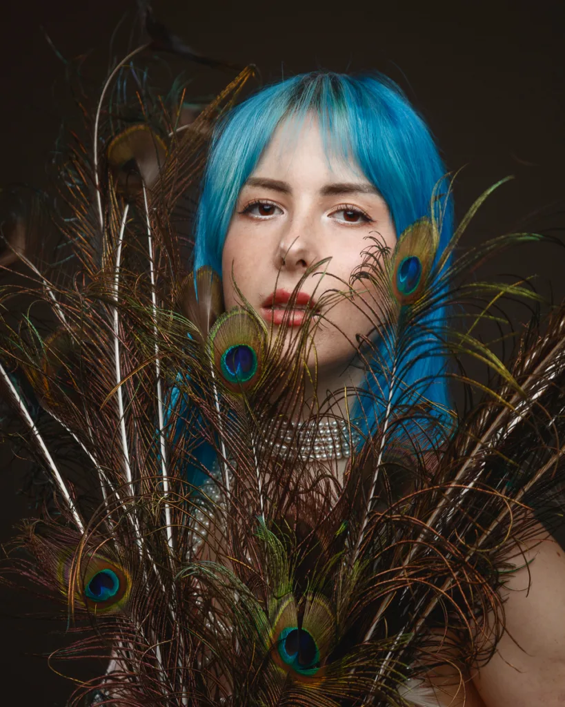 Person with blue hair holding peacock feathers