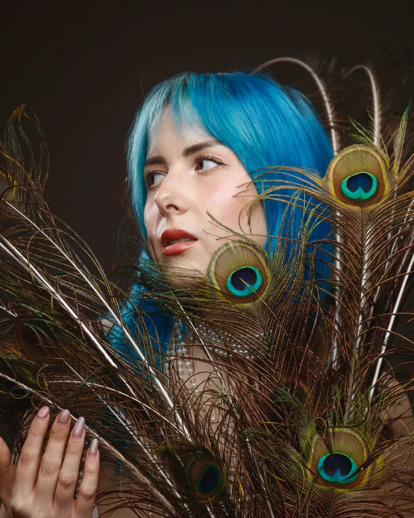 Woman with blue hair, holding peacock feathers.