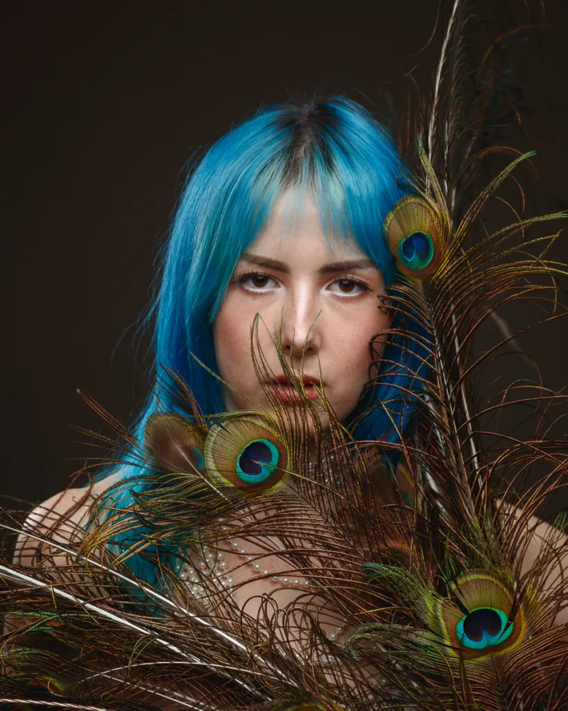 Person with blue hair holding peacock feathers