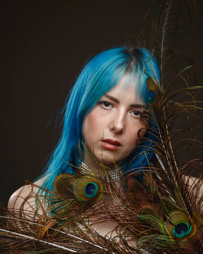 Woman with blue hair holding peacock feathers