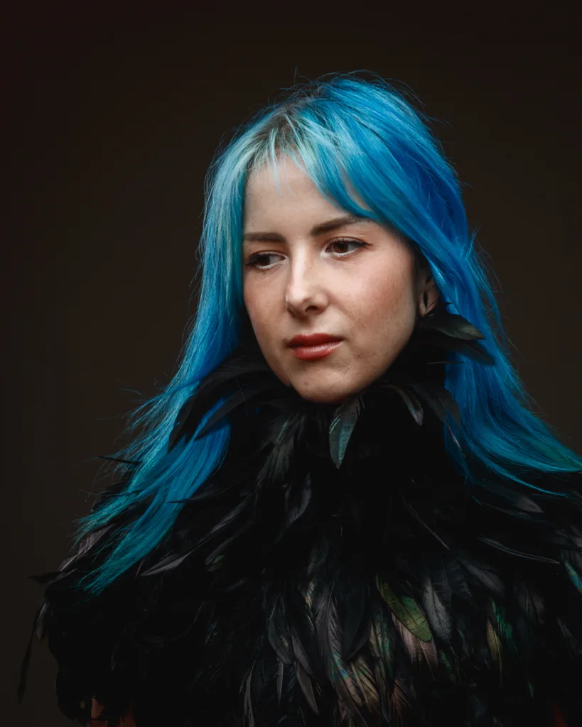 Person with blue hair and feathered outfit.