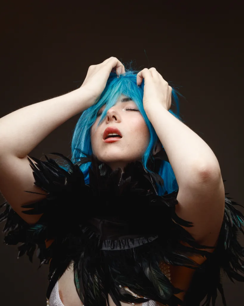 Woman with blue hair, feather clothing poses.