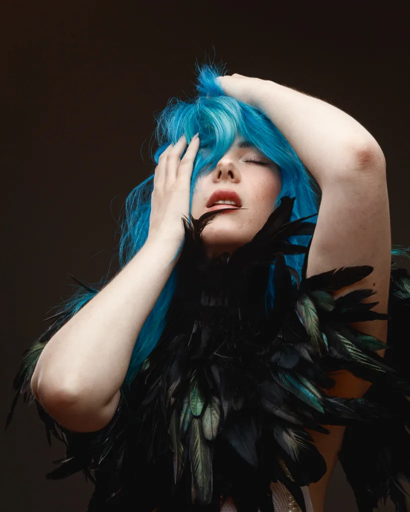 Person with blue hair and feathered outfit posing