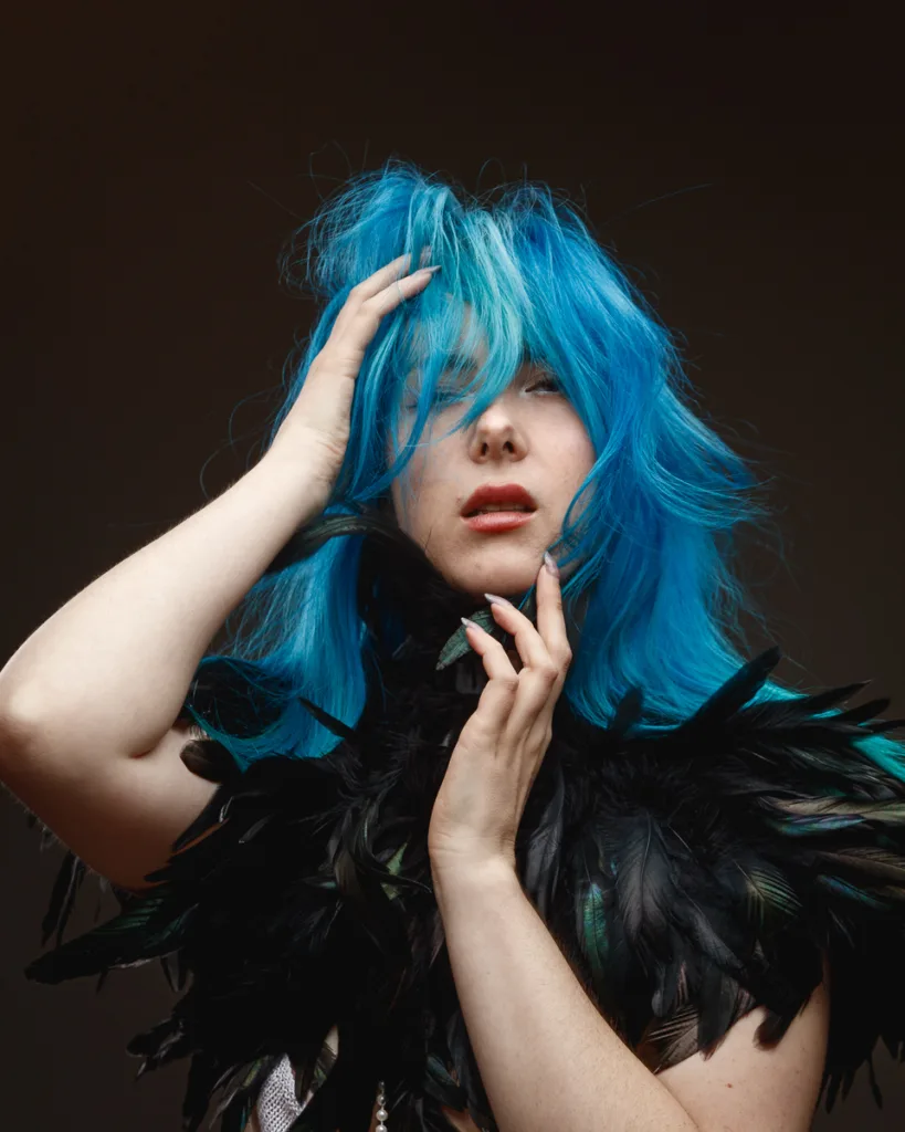 Person with blue hair wearing a feathered accessory.