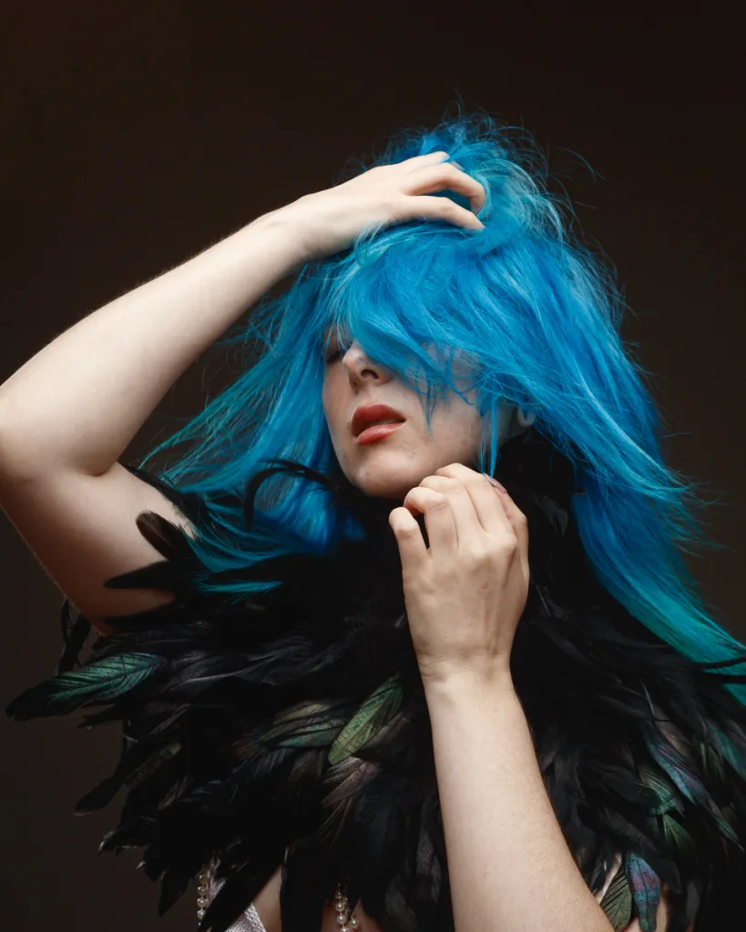 Person with vibrant blue hair and feathered collar.