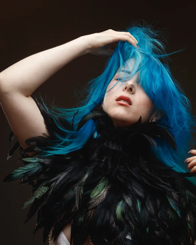 Person with vibrant blue hair and feather outfit.