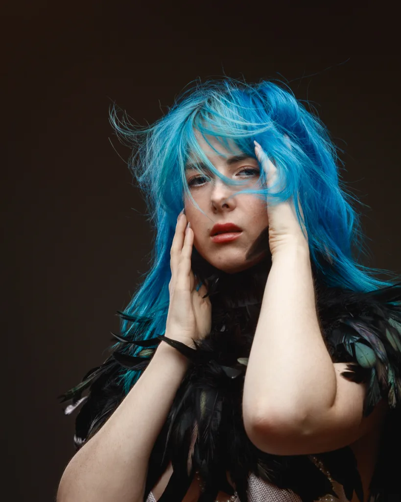Person with blue hair and feather outfit posing.