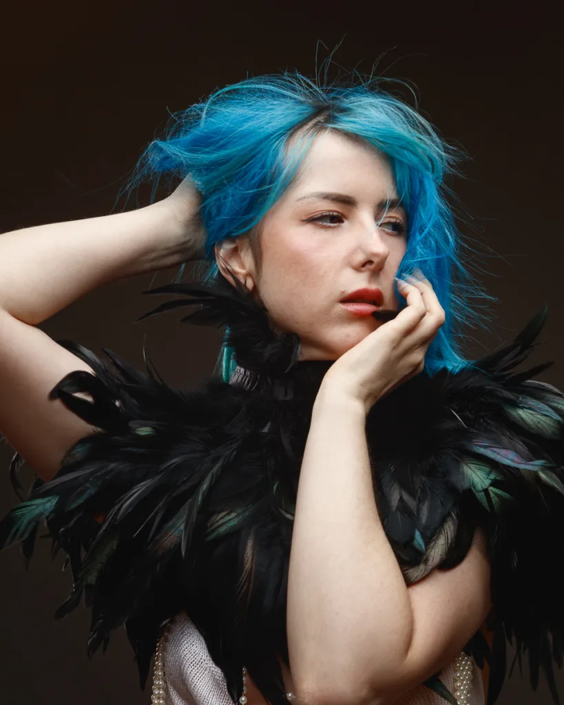 Person with blue hair and feathered outfit posing.