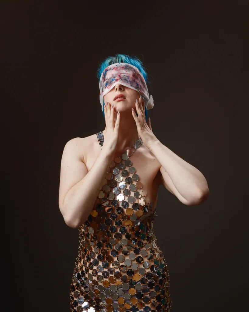 Person with blindfold, wearing metallic dress.
