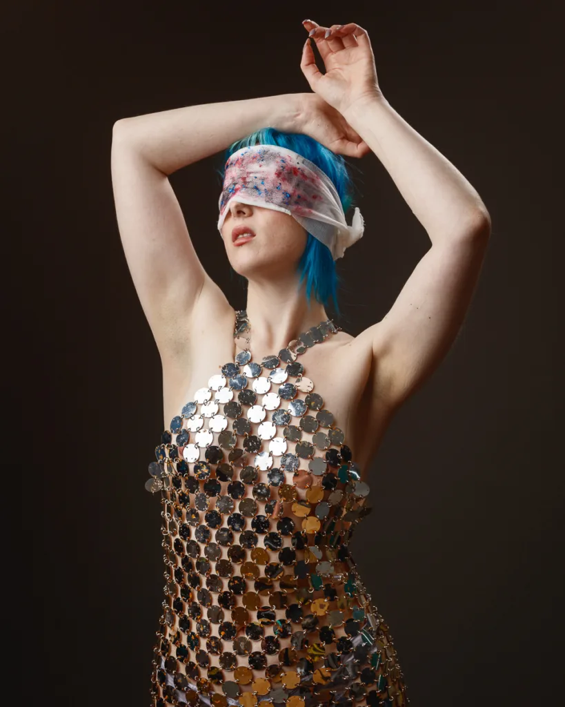 Person in shiny dress with blindfold, posing elegantly.