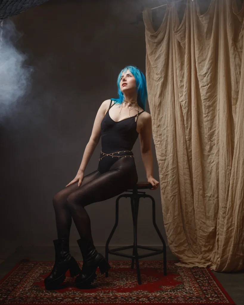 Person with blue hair posing on a stool.