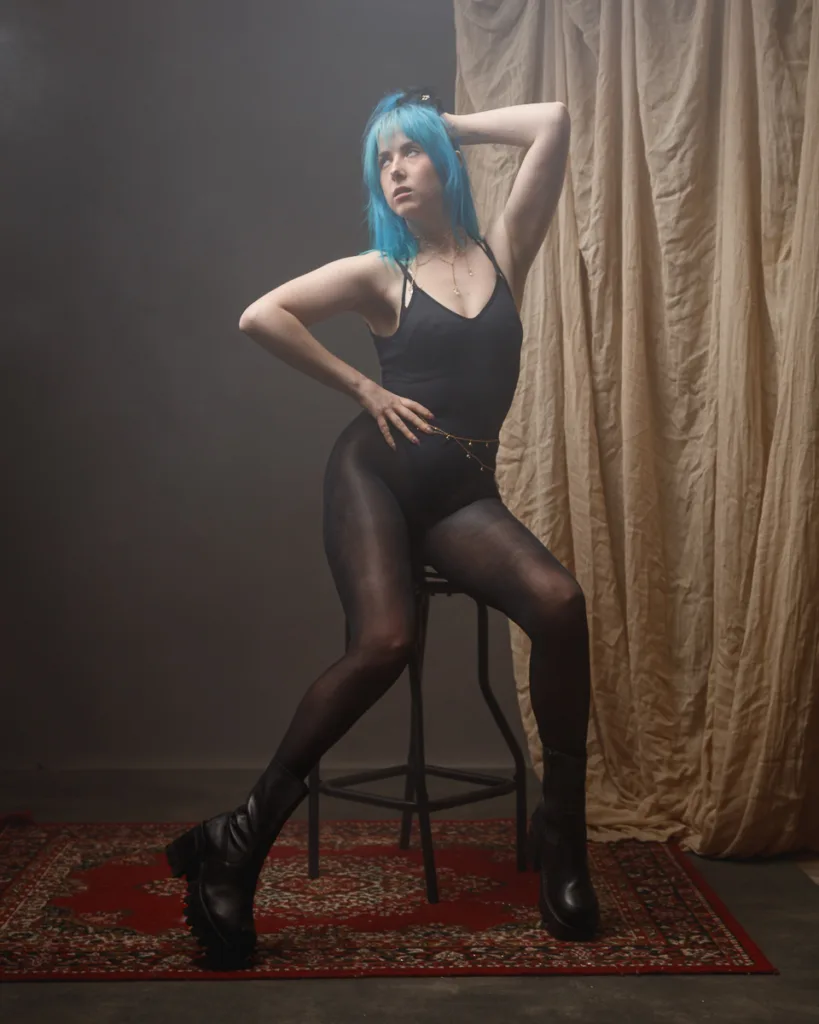 Person posing stylishly on a stool indoors.