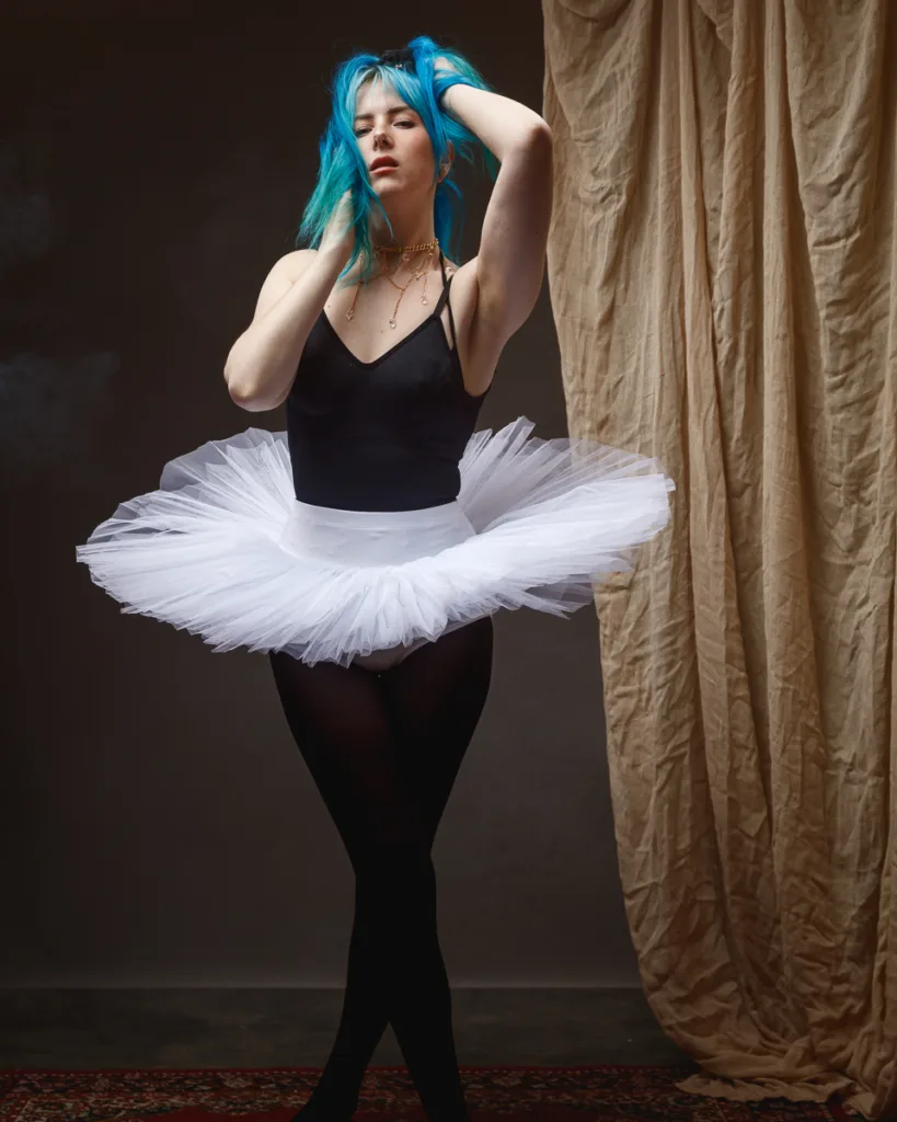 Ballerina with blue hair in white tutu poses.
