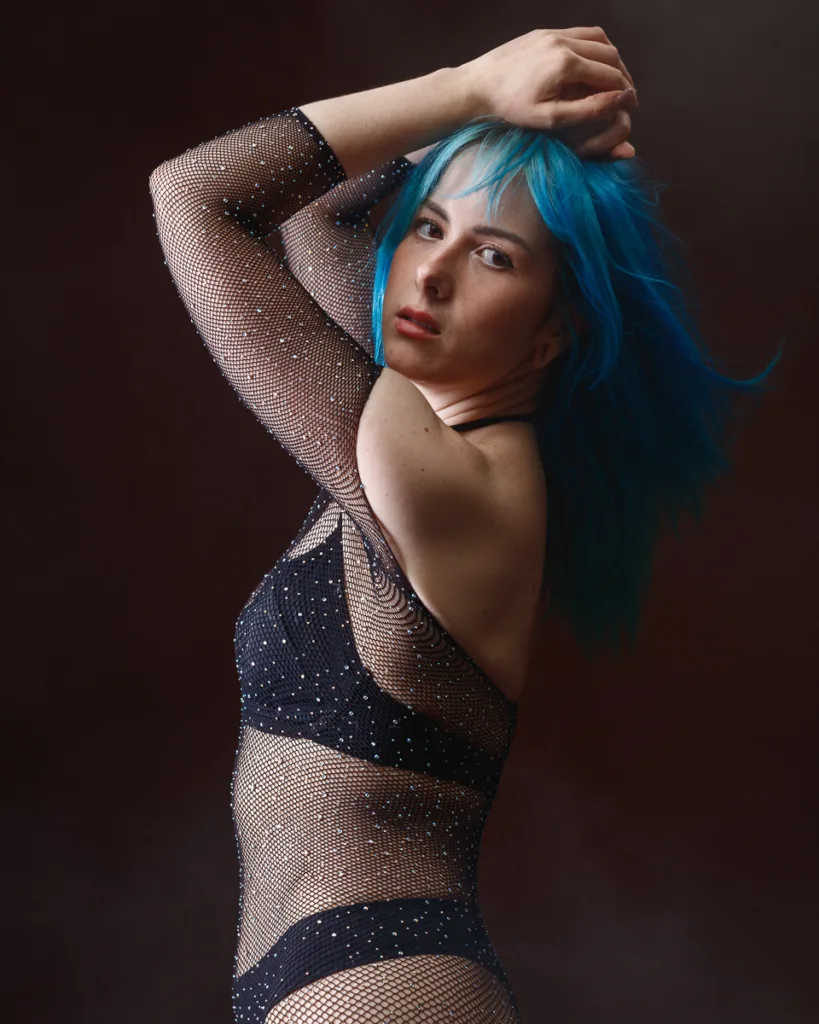 Woman with blue hair in mesh outfit posing elegantly.