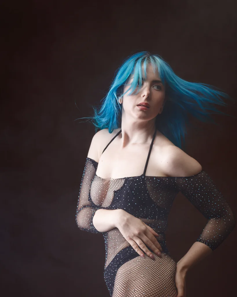 Woman with vibrant blue hair, wearing black mesh dress.
