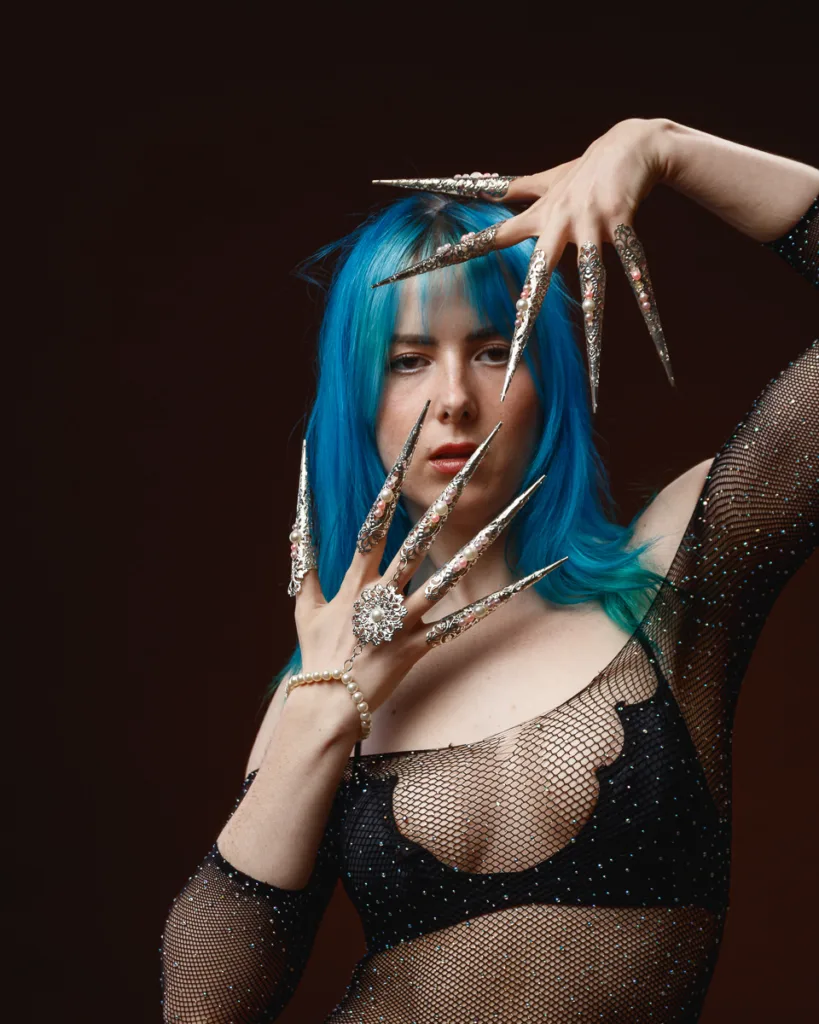 Person with blue hair and ornate long nails.
