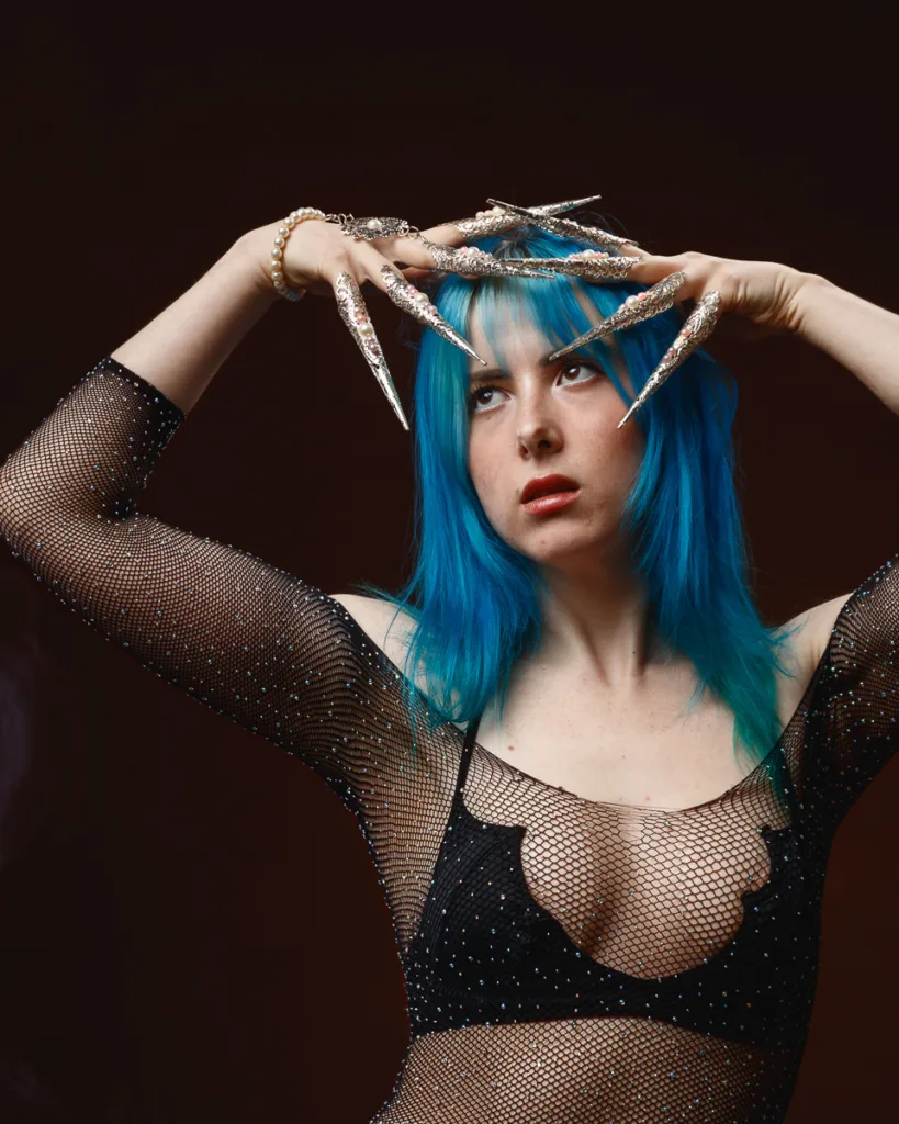 Woman with blue hair and elaborate nails posing.