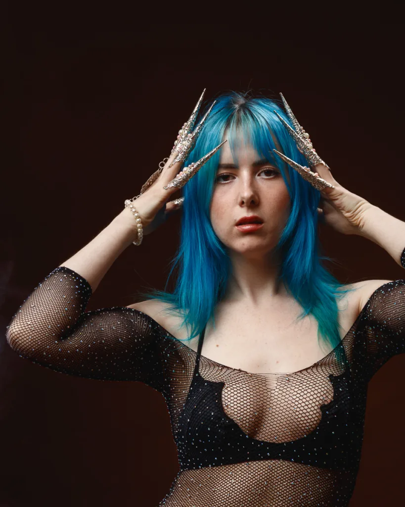 Woman in black mesh top, blue hair, decorative nails.