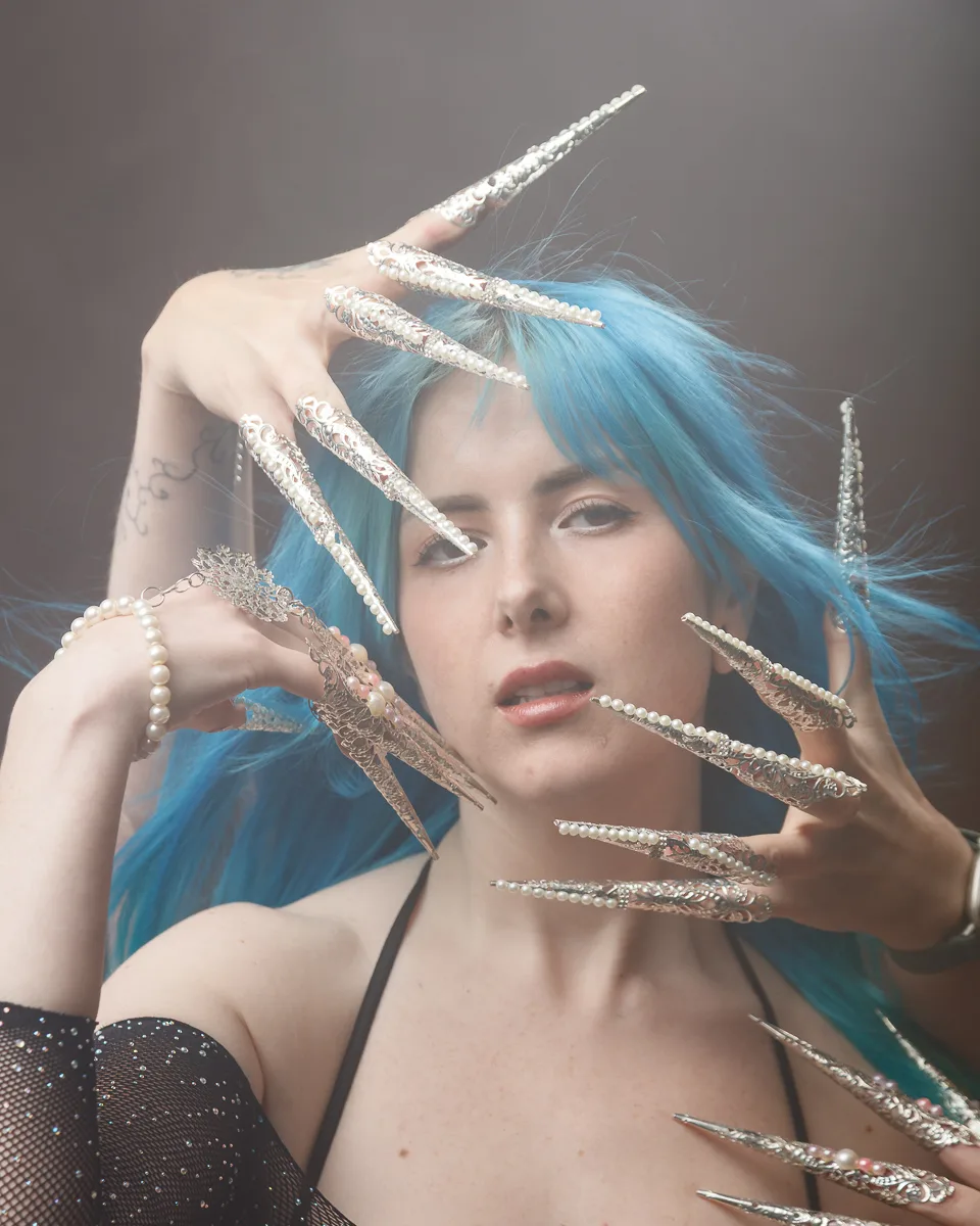 Model with blue hair, elaborate nail art display.