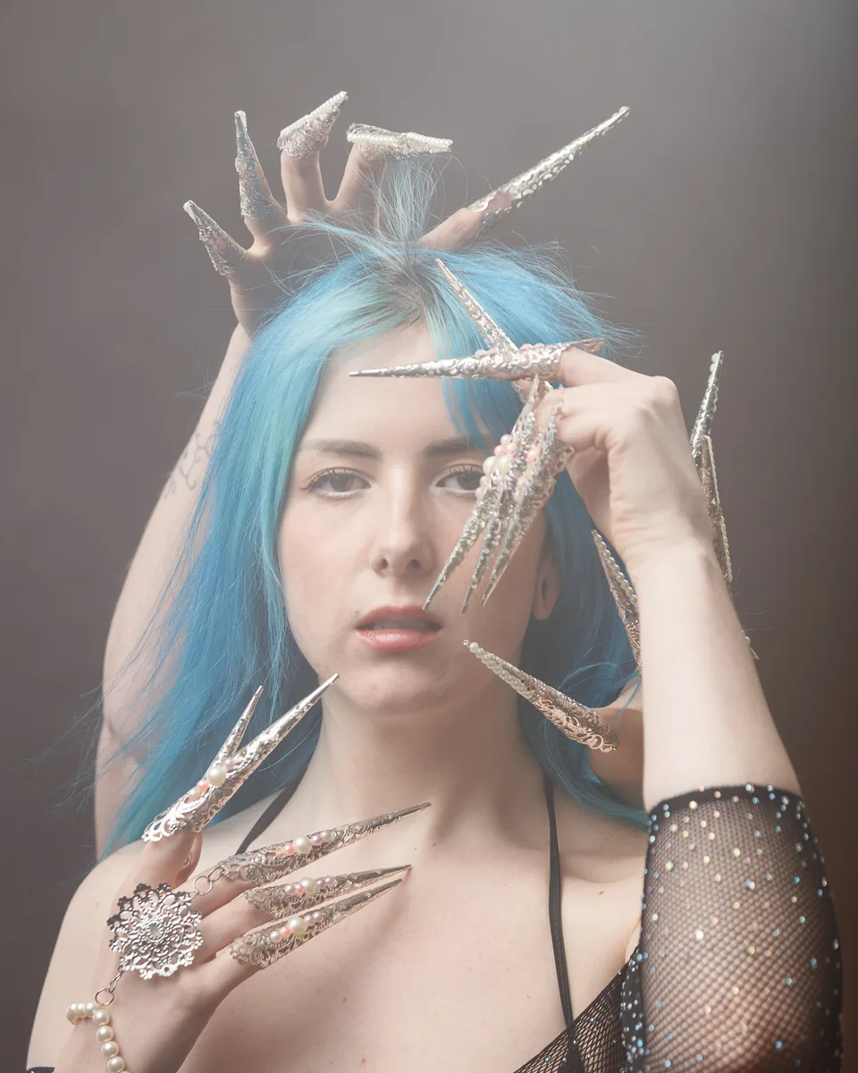 Woman with ornate long metallic nails and blue hair.