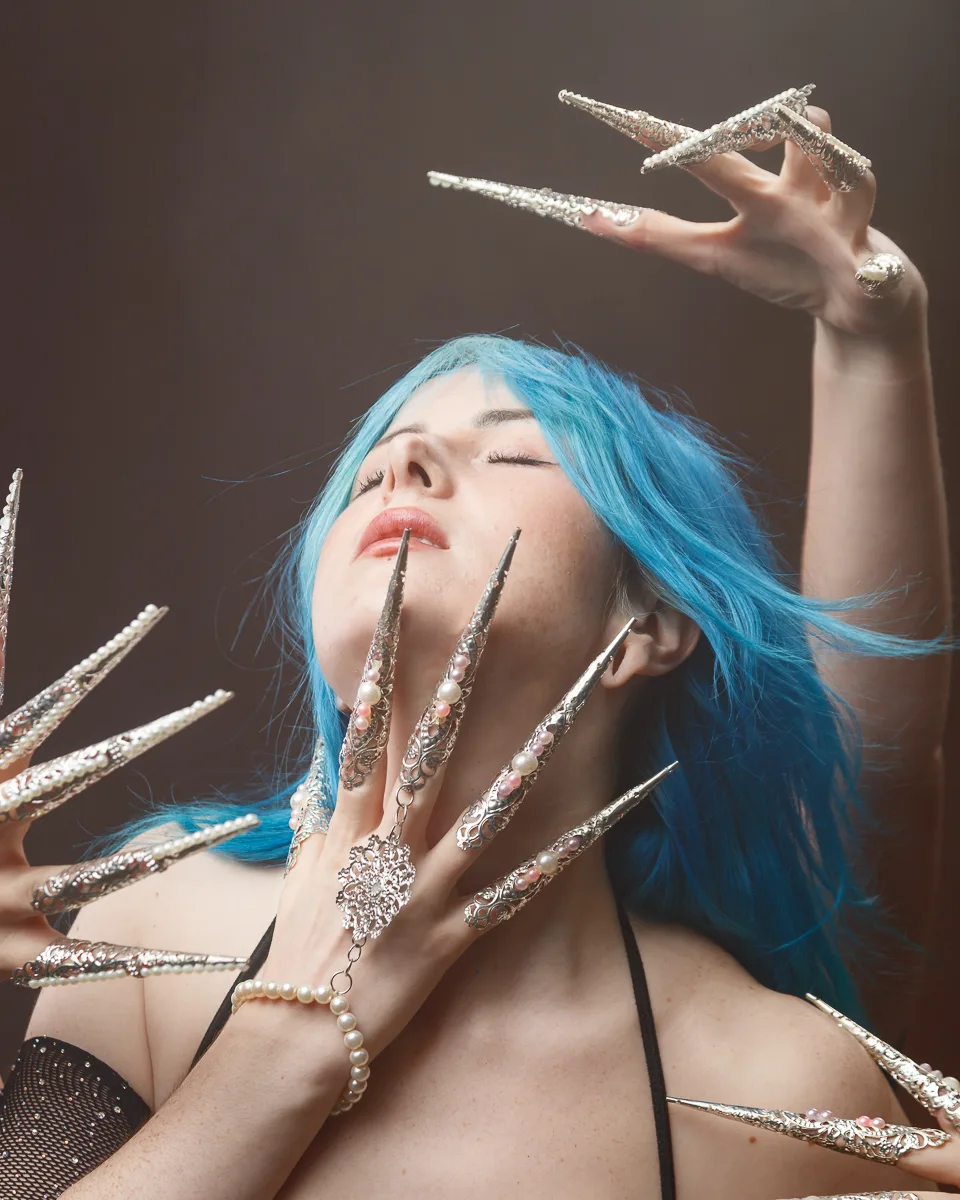 Woman with elaborate, metallic nail art and blue hair.