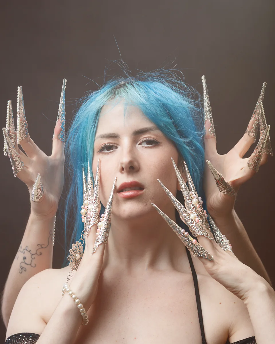 Person with blue hair wearing ornate silver nail extensions.