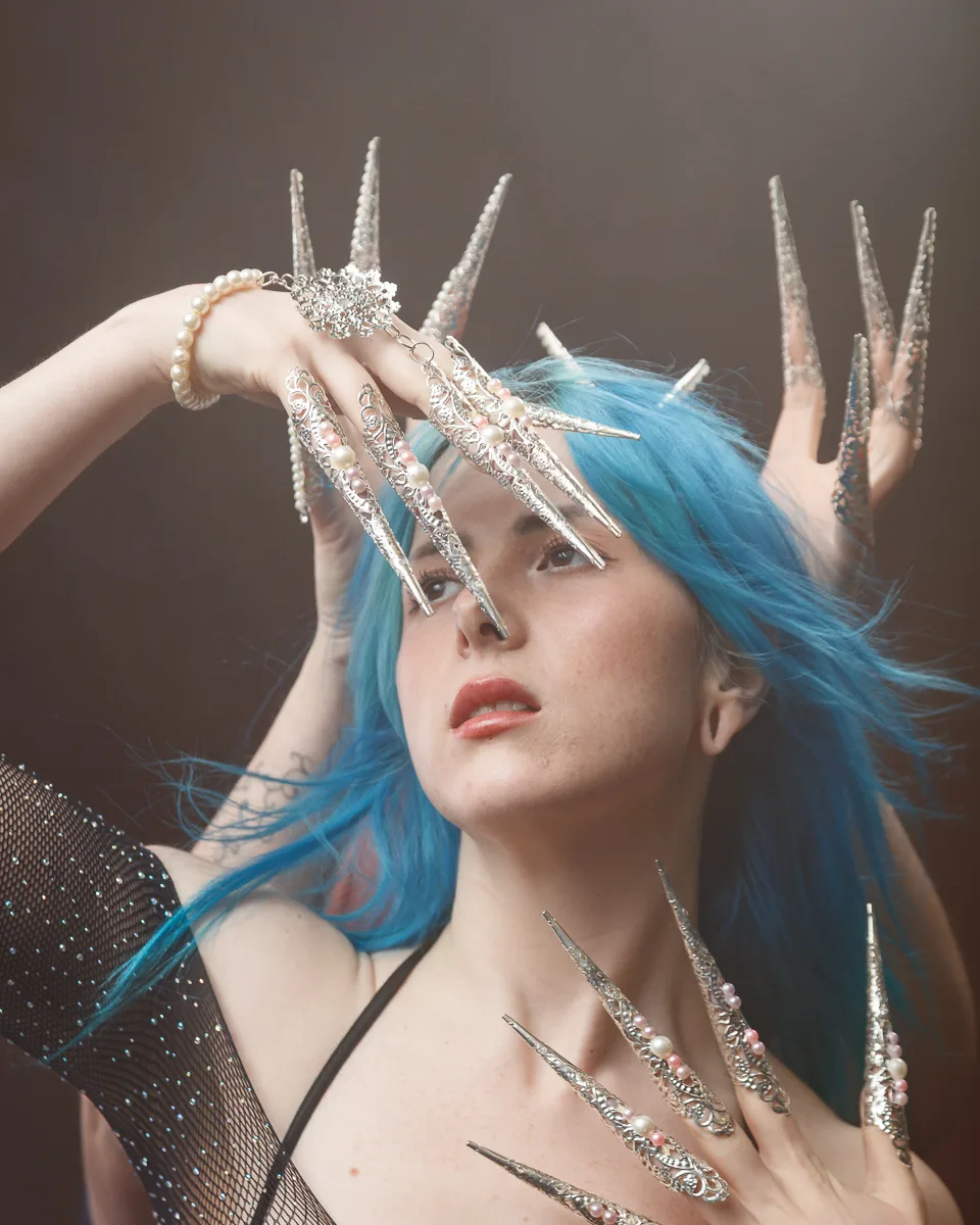 Person with blue hair and ornate silver finger extensions.