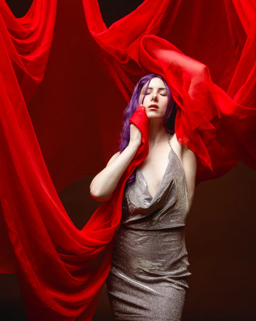 Woman in elegant dress posed with red fabric backdrop.