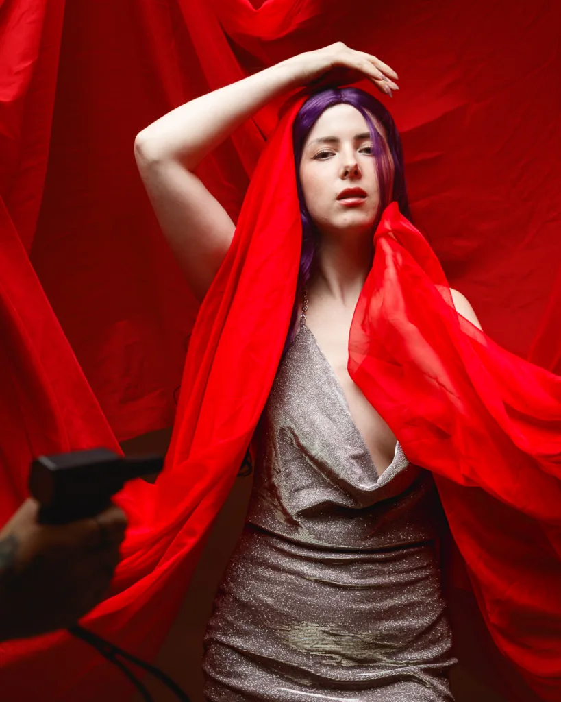 Woman in silver dress with red fabric backdrop.