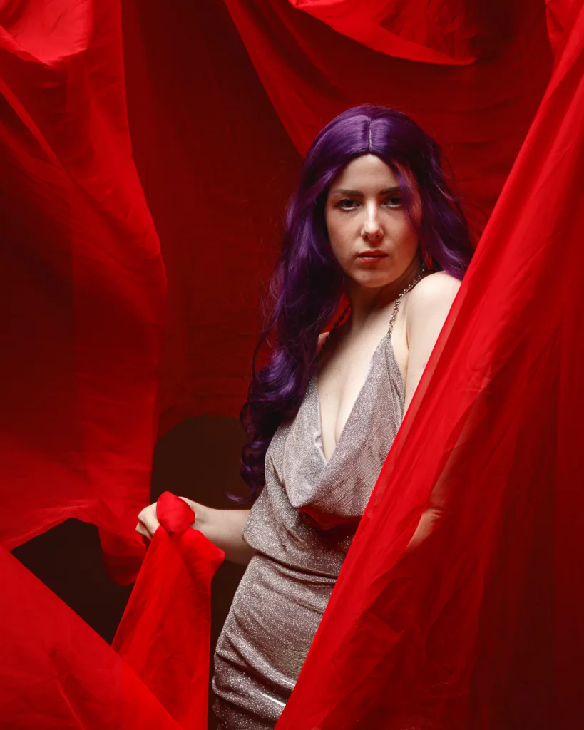 Woman with purple hair in red fabric setting.