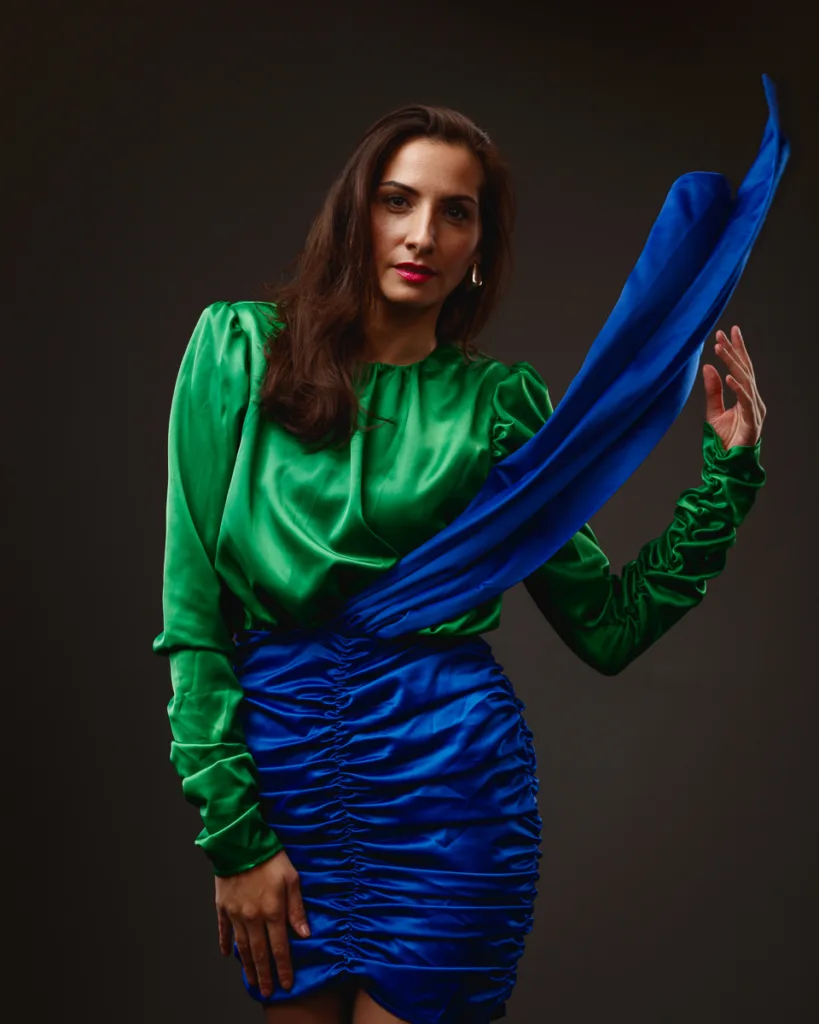 Woman wearing green blouse, blue skirt, posing elegantly.
