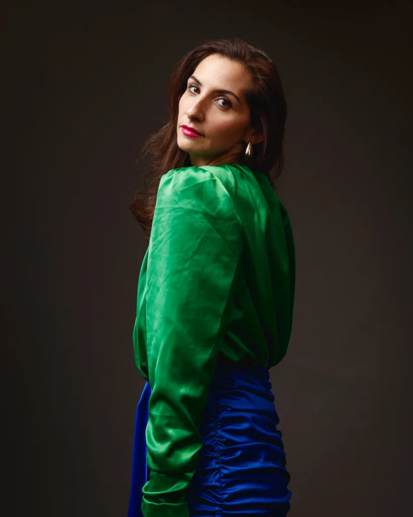 Woman back to camera in green blouse and blue skirt posing.