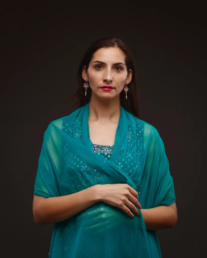 Woman in teal outfit with embroidered shawl.