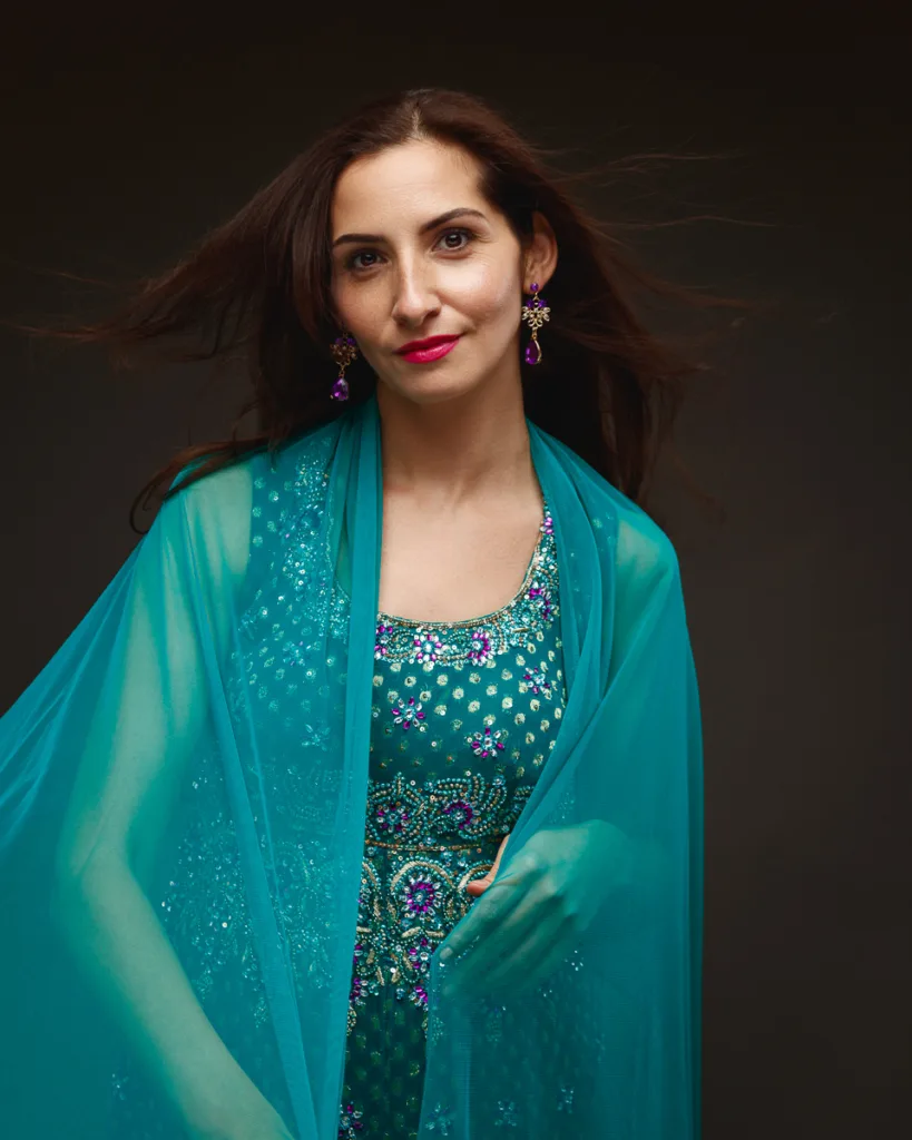 Woman in embellished teal dress with shawl and earrings.