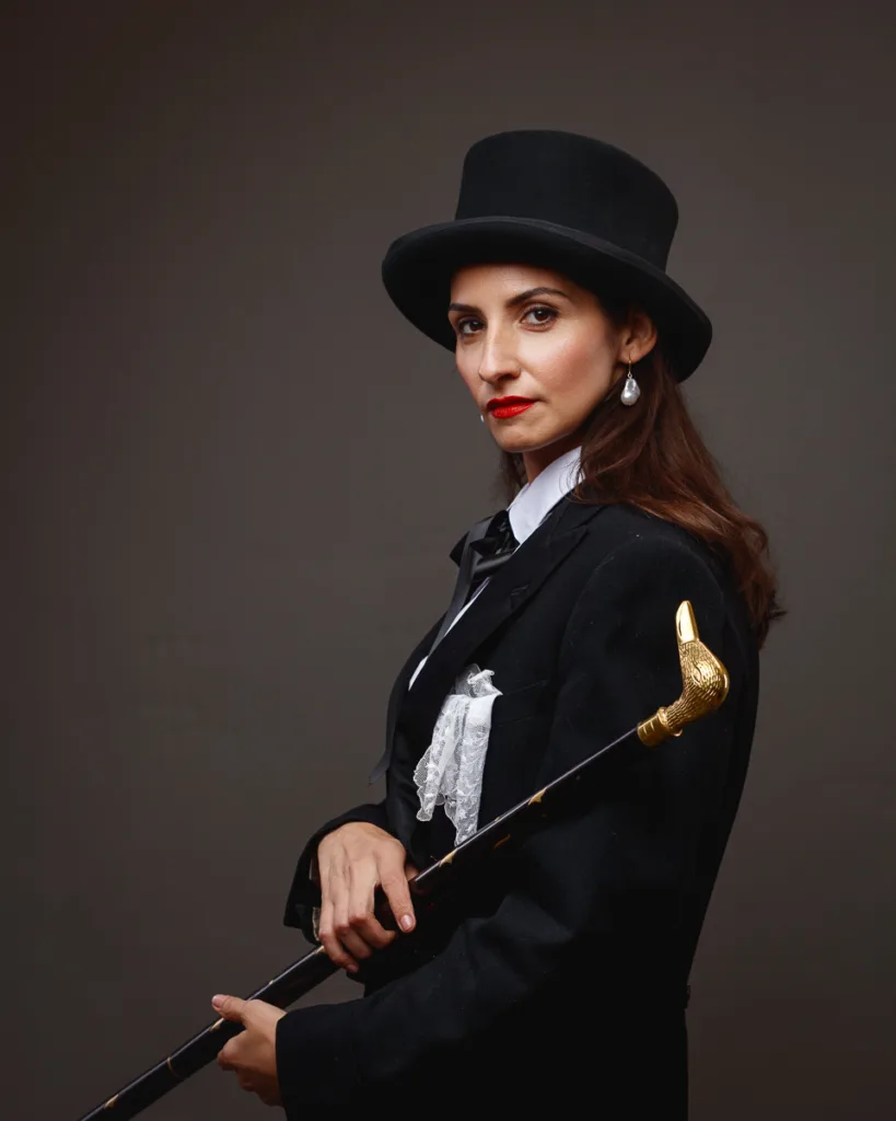 Woman in tuxedo and top hat holding cane.