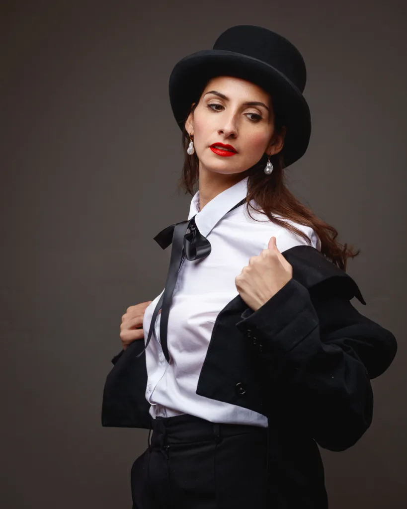 Woman in suit and bowler hat posing confidently.