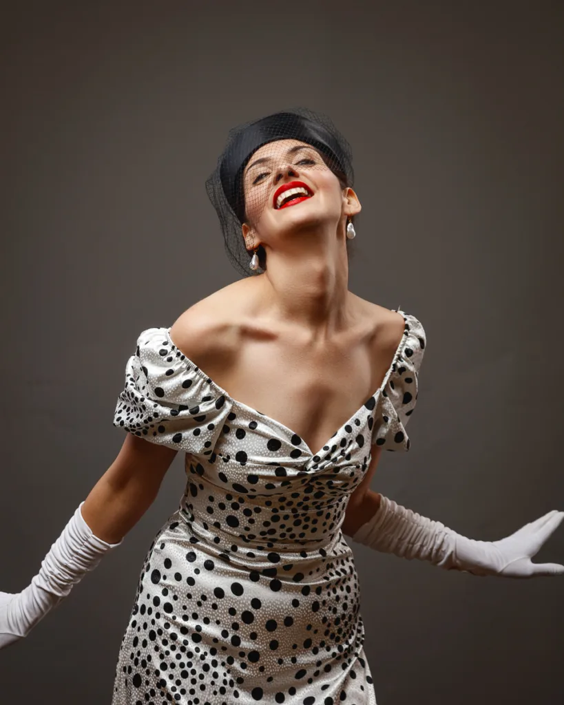 Woman in polka dot dress and gloves smiling.