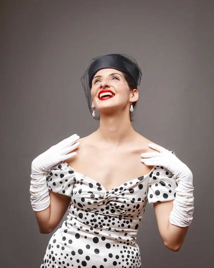 Woman smiling in polka dot dress and gloves.