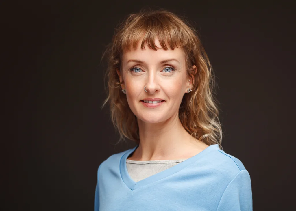 Smiling woman in blue top, neutral background.