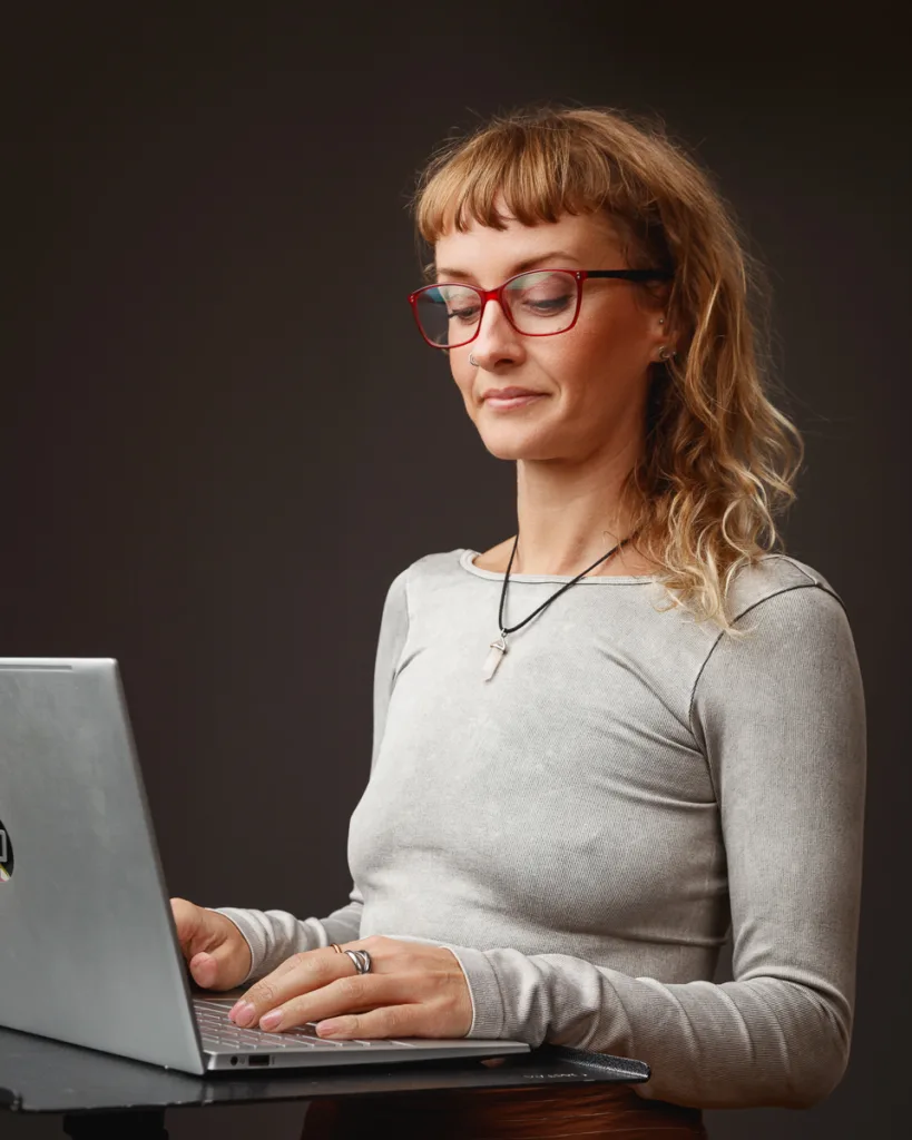 Person working on laptop with glasses and necklace.