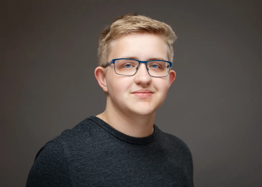 Smiling person wearing glasses and grey shirt.