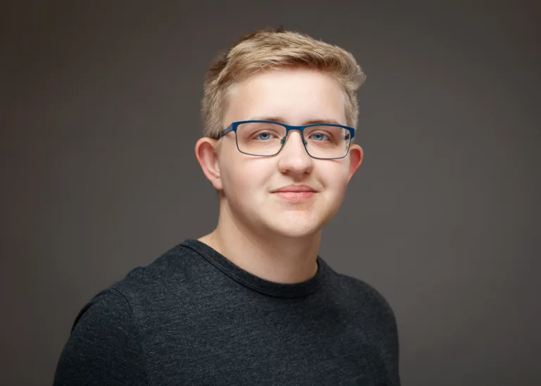 Smiling person wearing glasses and grey shirt.