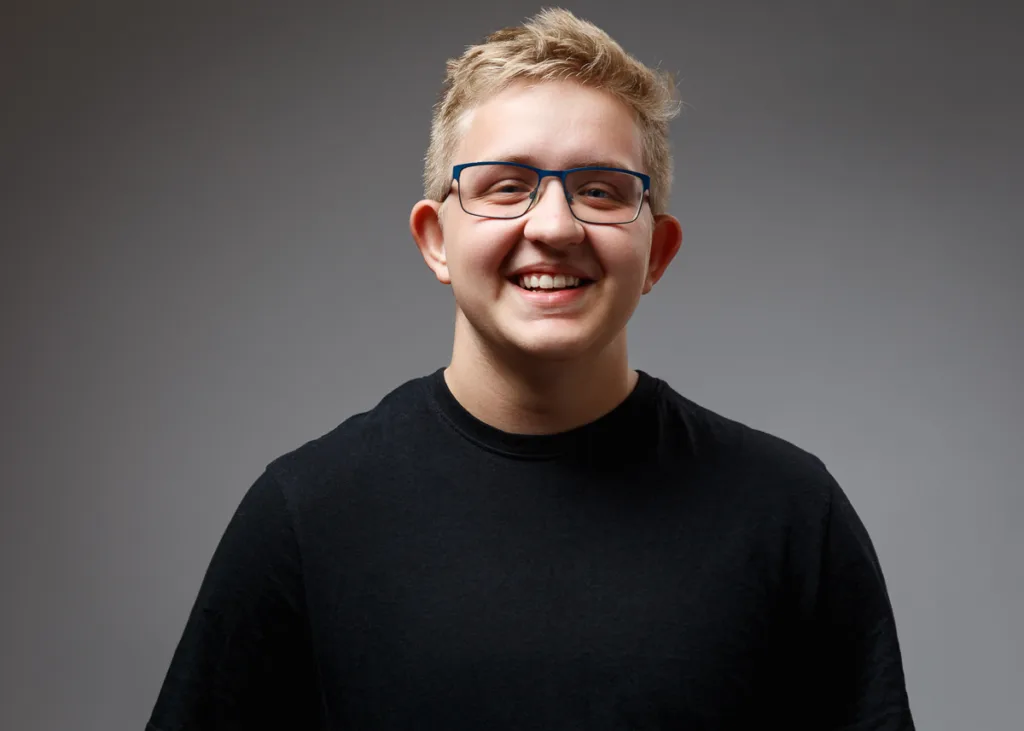 Smiling person with glasses and a black shirt.
