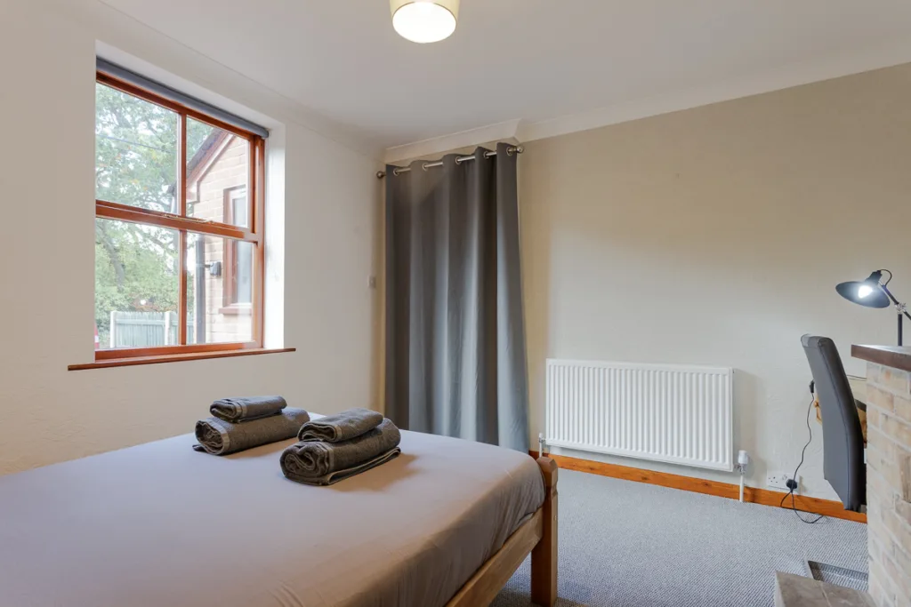 Minimalist bedroom with window, desk, and grey curtains.