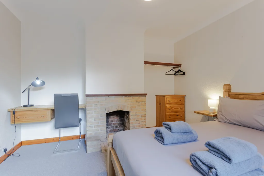 Cosy bedroom with desk, fireplace, and neatly folded towels.